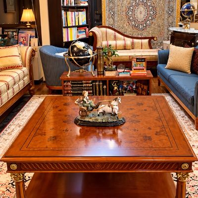 Sale Photo Thumbnail #69: Large square wooden coffee table with inlay detailing, carved legs, and gold accents, displayed alongside surrounding living room furniture and rugs.