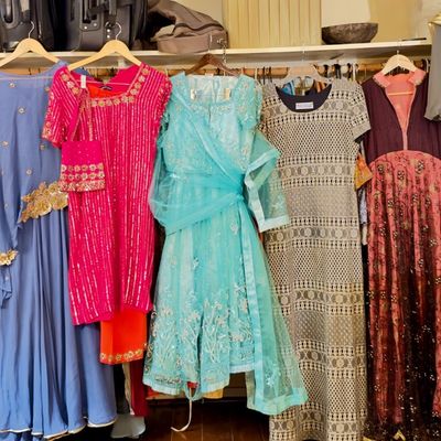 Sale Photo Thumbnail #68: A rack displaying a colorful collection of formal South Asian garments, including embellished lehengas, anarkalis, and salwar kameez sets in various fabrics.