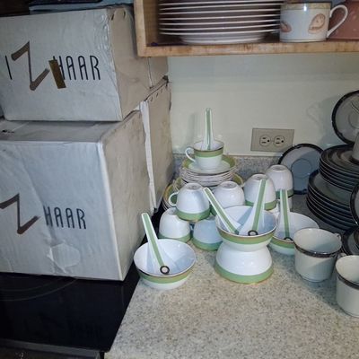 Sale Photo Thumbnail #107: Collection of porcelain dinnerware including green-trimmed tea sets with matching soup spoons, dark-rimmed china pieces, and original Izhaar packaging boxes.