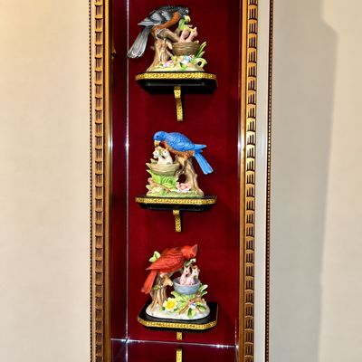 Sale Photo Thumbnail #79: Gilt-framed wall shadow box with red velvet backing, displaying three porcelain bird figurines on tier shelves.