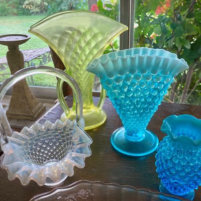 Collection of vintage art glass pieces, including Fenton-style blue Hobnail vases, a clear opalescent glass basket, and a yellow Vaseline...