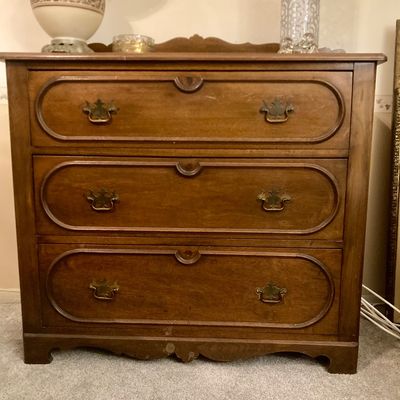Traditional wooden three-drawer chest featuring recessed oval molded panels, ornate brass bail handles, and a scalloped base apron.