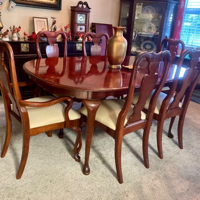 Traditional cherry dining room set featuring an oval pedestal table with Queen Anne style legs and six matching splat-back chairs with...