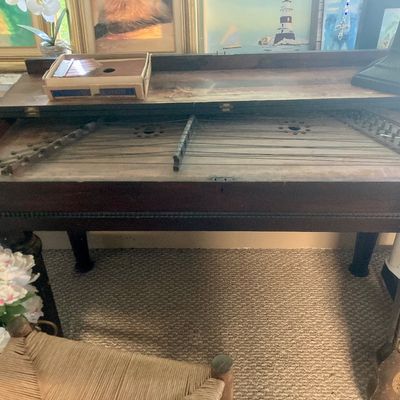 Antique wooden hammered dulcimer housed inside a dark stain table cabinet with turned legs.