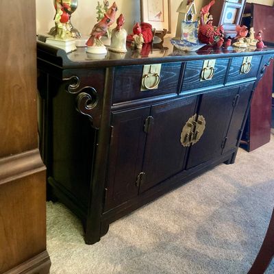Asian-style dark wood sideboard featuring decorative brass hardware, carved scroll side details, and four cabinet doors topped with drawers.