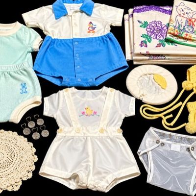 Sale Photo Thumbnail #22: Collection of vintage baby clothing and linens, including embroidered rompers, yellow knit hat with matching booties, plastic diaper covers, and hand-embroidered textiles.