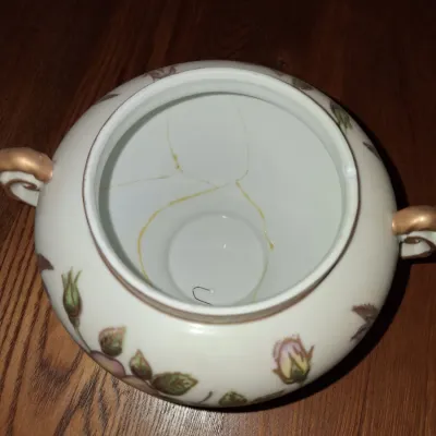 Sale Photo Thumbnail #636: Antique porcelain double-handled sugar bowl featuring hand-painted floral rose motifs and gilt handles. Note significant internal repair and cracking visible inside the bowl.