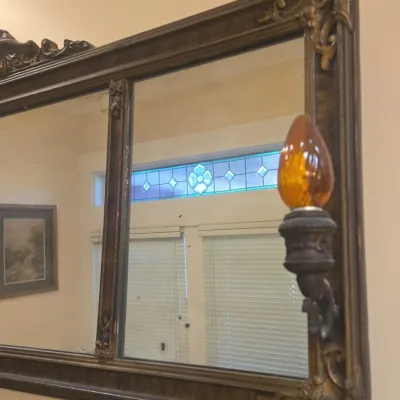 Sale Photo Thumbnail #528: Vintage ornate gold-framed wall mirror featuring attached sconces with amber glass light bulbs.