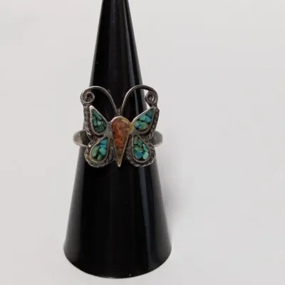 Sale Photo Thumbnail #799: Vintage Southwest-style sterling silver butterfly ring featuring crushed turquoise and coral inlay, displayed on a black ring cone.