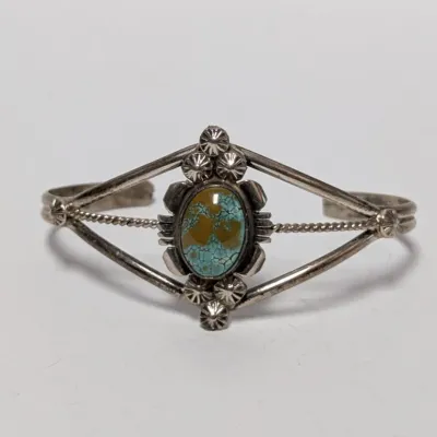 Sale Photo Thumbnail #818: Vintage Southwest sterling silver cuff bracelet featuring a central oval turquoise cabochon with spiderweb matrix, fluted rain drops, and twisted wire accents.
