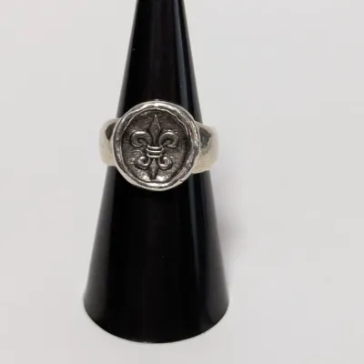 Sale Photo Thumbnail #798: Sterling silver fleur-de-lis seal ring displayed on a black ring cone.
