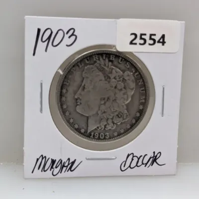 Sale Photo Thumbnail #879: 1903 Morgan silver dollar encased in a cardboard coin flip labeled with handwritten text and a lot sticker.