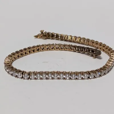 Sale Photo Thumbnail #816: Gold-tone tennis bracelet set with clear cubic zirconia stones, featuring a box clasp with safety latch.
