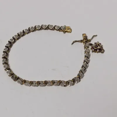 Sale Photo Thumbnail #820: Diamond S-link tennis bracelet featuring a gold-tone box clasp and an attached small heart-shaped dangling charm with red stones.