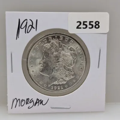 Sale Photo Thumbnail #883: 1921 Morgan silver dollar, housed in a cardboard flip holder with handwritten and printed lot labels.