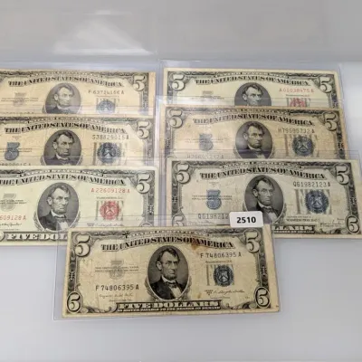 Sale Photo Thumbnail #835: Collection of seven vintage US $5 currency notes, including silver certificates and United States notes, each housed in protective clear plastic sleeves.