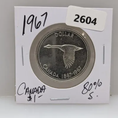 Sale Photo Thumbnail #929: 1967 Canadian silver dollar coin commemorating the centennial of Confederation, housed in a cardboard flip holder.