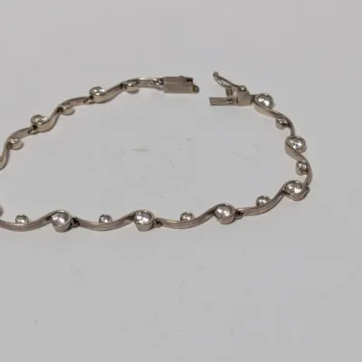 Sale Photo Thumbnail #822: Silver-tone wavy link tennis bracelet set with round clear stones and a secure box clasp.