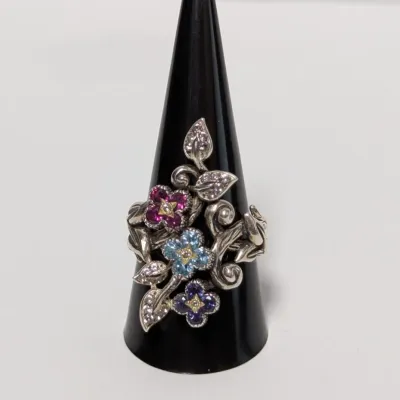 Sale Photo Thumbnail #800: Sterling silver floral bypass ring featuring colorful pave-set gemstone flowers and pave leaf accents, displayed on a black ring cone.