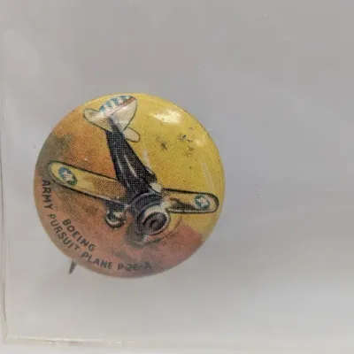 Sale Photo Thumbnail #115: Vintage Boeing Army Pursuit Plane P-26-A pinback button housed in a protective sleeve, featuring colorful airplane illustration and minor age-related wear.