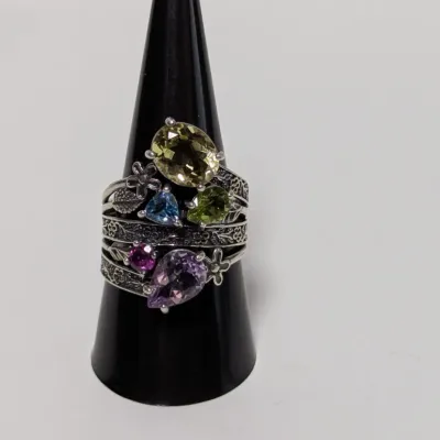 Sale Photo Thumbnail #797: Set of stacked sterling silver floral motif rings featuring multi-colored faceted gemstones, displayed on a black ring cone.