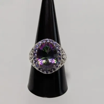 Sale Photo Thumbnail #790: Sterling silver cocktail ring featuring a large oval mystic topaz gemstone surrounded by a halo of small purple accent stones and filigree side details.