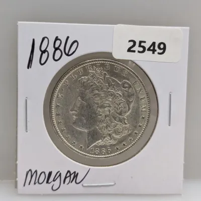 Sale Photo Thumbnail #874: 1886 Morgan silver dollar coin displayed in a cardboard flip holder.