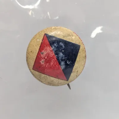 Sale Photo Thumbnail #36: Vintage small round pinback button featuring a red and dark blue diamond logo on a light background, showing surface wear and age patina.