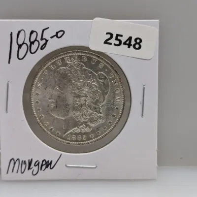 Sale Photo Thumbnail #873: 1885-O Morgan silver dollar coin, housed in a protective cardboard flip holder.