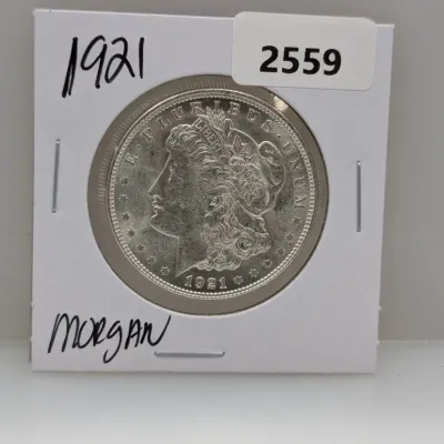 Sale Photo Thumbnail #884: 1921 Morgan silver dollar coin housed in a cardboard flip holder.