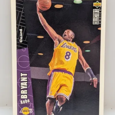 Sale Photo Thumbnail #606: 1996-97 Upper Deck Collector's Choice Kobe Bryant rookie basketball card #267, featuring Bryant driving to the basket in his Los Angeles Lakers jersey.
