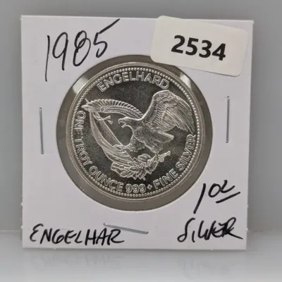 Sale Photo Thumbnail #859: 1985 Engelhard 1 troy ounce .999 fine silver round featuring an American eagle motif, packaged in a cardboard coin flip holder.