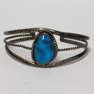 Sale Photo Thumbnail #823: Vintage Native American style sterling silver cuff bracelet, featuring a central oval turquoise cabochon set in a twisted wire bezel with stamped details.