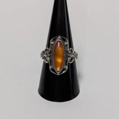 Sale Photo Thumbnail #810: Vintage sterling silver ring featuring a marquise-cut amber cabochon set in an ornate scrollwork bezel, displayed on a black ring stand.