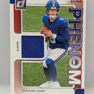 Sale Photo Thumbnail #567: Panini Donruss Rookie Phenom Jaxson Dart trading card featuring a player-worn jersey relic swatch. The card displays Dart in his New York Giants uniform with 'Phenom' embossed down the right side.