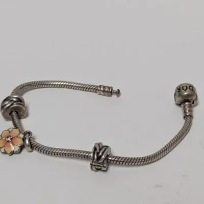 Sale Photo Thumbnail #817: Pandora sterling silver charm bracelet featuring a barrel clasp, knot spacers, and an enamel flower charm.