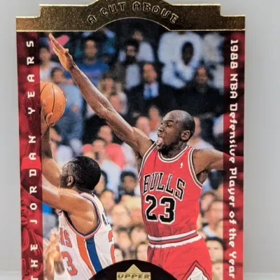 Sale Photo Thumbnail #307: Upper Deck Michael Jordan 'A Cut Above' trading card, highlighting his 1988 NBA Defensive Player of the Year achievement. The die-cut die-struck card features gold foil detailing and is in good condition.