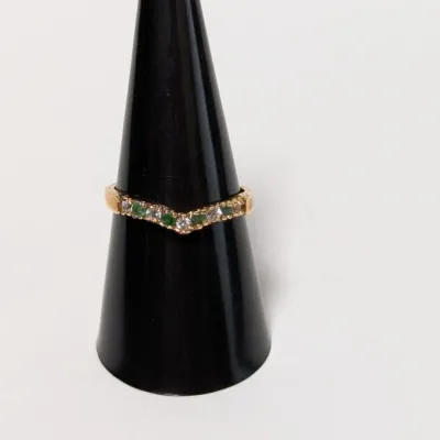 Sale Photo Thumbnail #806: Gold V-shaped chevron ring set with small green emeralds and clear stones, displayed on a black ring stand.