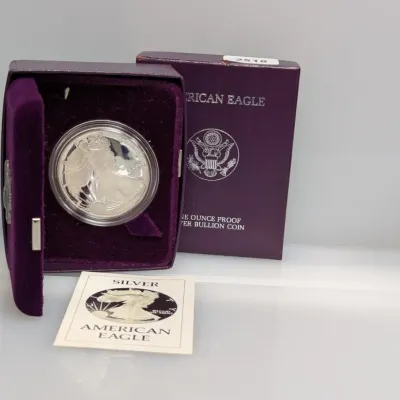 Sale Photo Thumbnail #843: American Eagle one-ounce proof silver bullion coin in a clear capsule, housed in its original purple velvet display case and outer box with Certificate of Authenticity.
