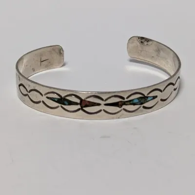 Sale Photo Thumbnail #812: Native American style sterling silver cuff bracelet featuring stamped geometric designs and small inlaid turquoise accent stones.
