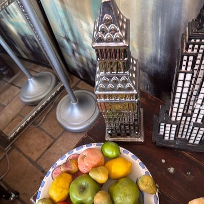 Sale Photo Thumbnail #40: A colorful ceramic bowl filled with artificial fruit, displayed alongside metallic architectural skyline sculptures on a wooden table.