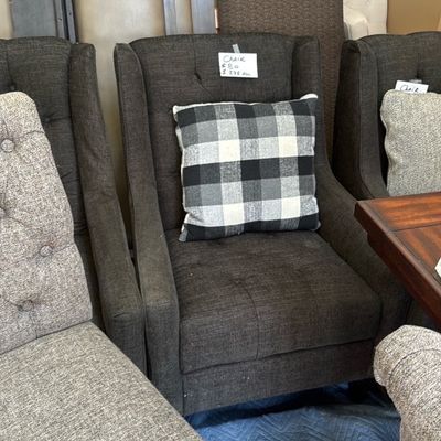 Sale Photo Thumbnail #35: Modern charcoal grey tufted wingback armchair paired with a black-and-white buffalo plaid throw pillow, displayed alongside additional upholstered dining chairs.