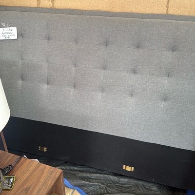 Sale Photo Thumbnail #27: Modern tufted gray upholstered king headboard resting on a protective moving blanket, accompanied by a mid-century style wooden nightstand.