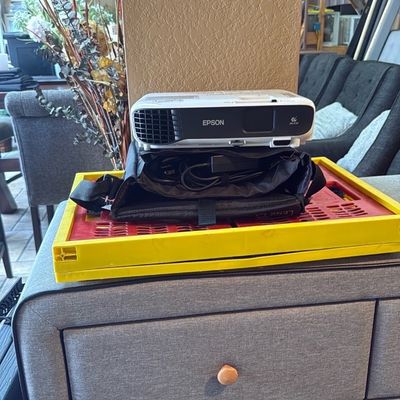 Sale Photo Thumbnail #25: Compact white Epson digital projector resting on a black carrying case with cables, stacked on a yellow frame.