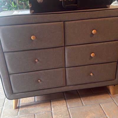 Sale Photo Thumbnail #15: Modern mid-century style gray fabric-upholstered six-drawer dresser with wooden knobs and splayed feet, topped with an open saxophone case.
