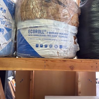 Sale Photo Thumbnail #34: Unopened roll of Knauf EcoRoll fiberglass insulation with formaldehyde-free ECOSE technology sitting on a wooden shelf.