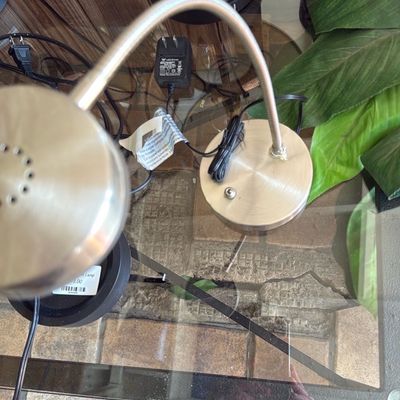 Sale Photo Thumbnail #32: Brushed nickel gooseneck desk lamp sitting on a glass-top table.