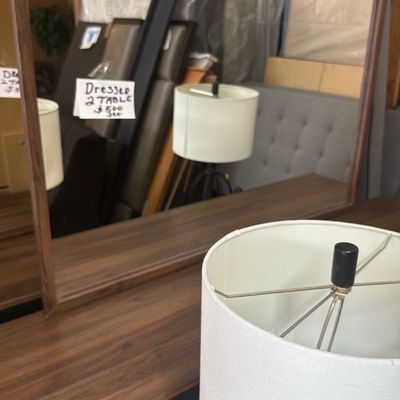 Sale Photo Thumbnail #26: Mid-century modern style walnut dresser with attached rectangular mirror and dark accent drawer, accompanied by a table lamp with a white drum shade.