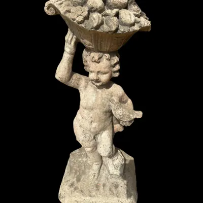 Sale Photo Thumbnail #400: Classic cast concrete standing garden statue of a cherub holding a bird and balancing a heavy cornucopia fruit basket overhead on a square pedestal base.  