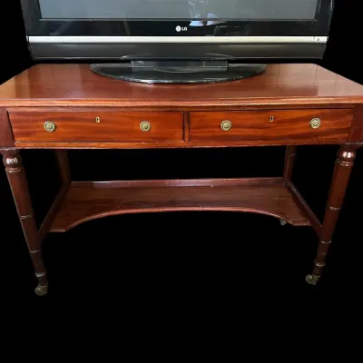 Sale Photo Thumbnail #584: Rectangular mahogany desk featuring 2 front drawers with rosette brass knobs  keyhole accents  turned spindle legs on brass caster wheels  and a curved lower stretcher shelf. (TV pictured on top not included). 